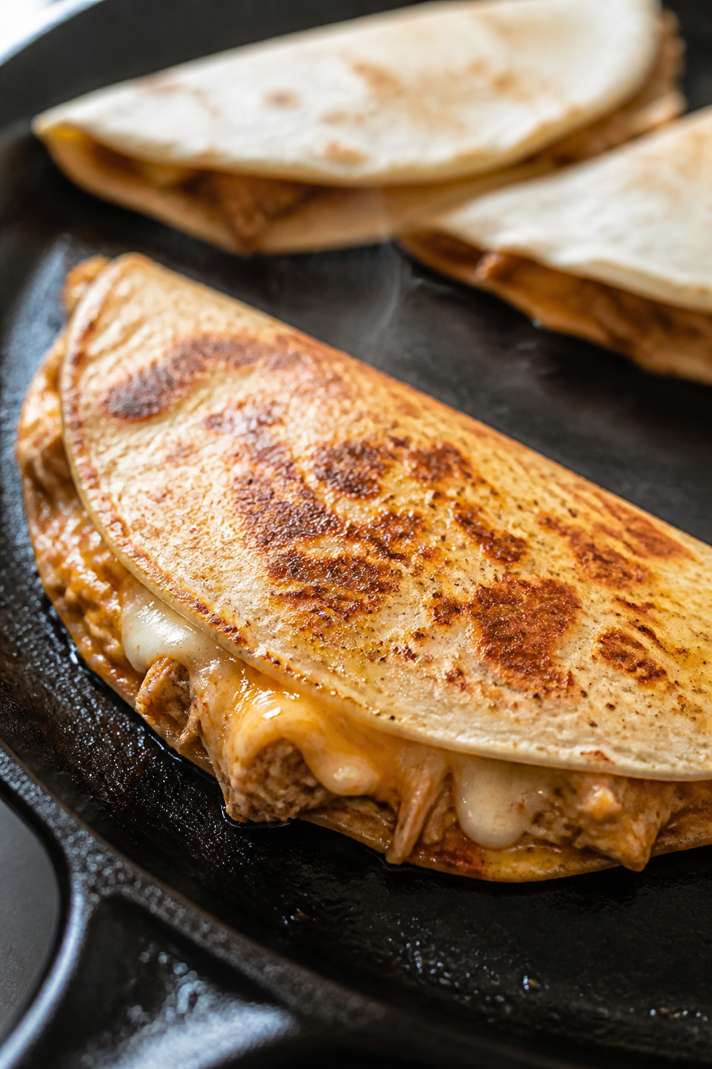 Close-up detail: A folded rotisserie chicken quesadilla melt sizzling in a cast-iron skillet mid-coo