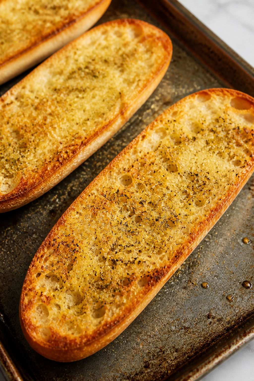 Close-up detail: Golden, par-baked French bread halves on a preheated sheet pan, cut sides up, edges