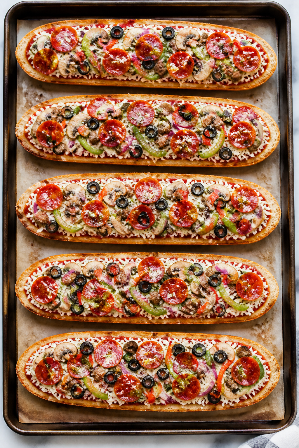Cooking process action: Overhead shot of assembled French bread pizzas just before the final bake—