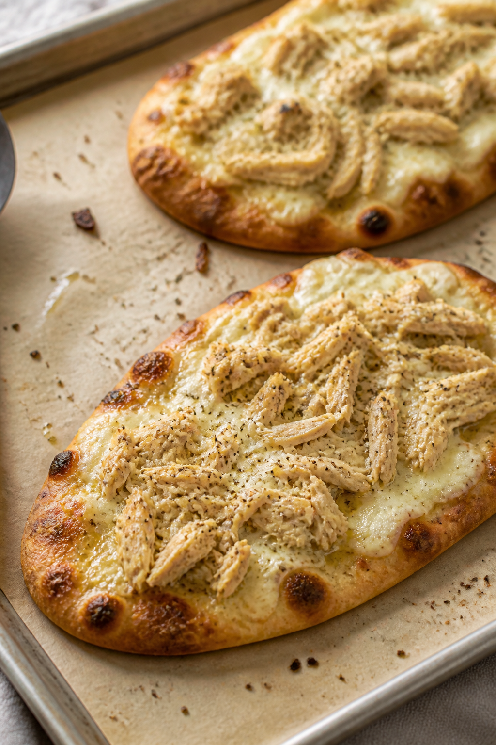Cooking process close-up: Flatbreads on a parchment-lined sheet pan just out of a 425°F oven, edges