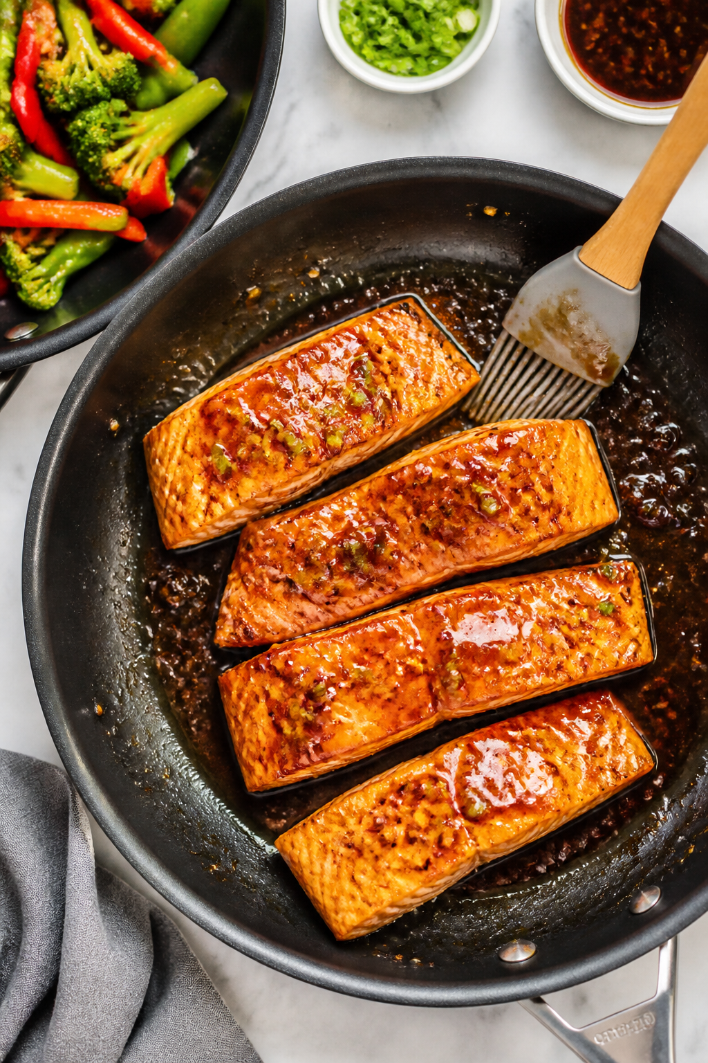 Cooking process: Overhead shot of salmon fillets in a large nonstick skillet mid-glaze, sauce bubbli