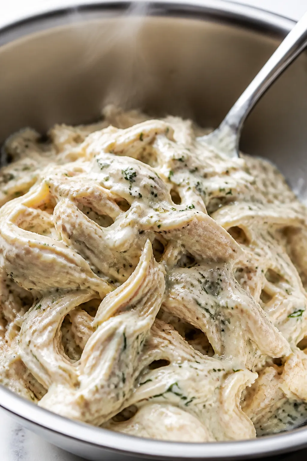 Close-up detail of ranch-coated shredded chicken just tossed in a stainless mixing bowl, glistening 