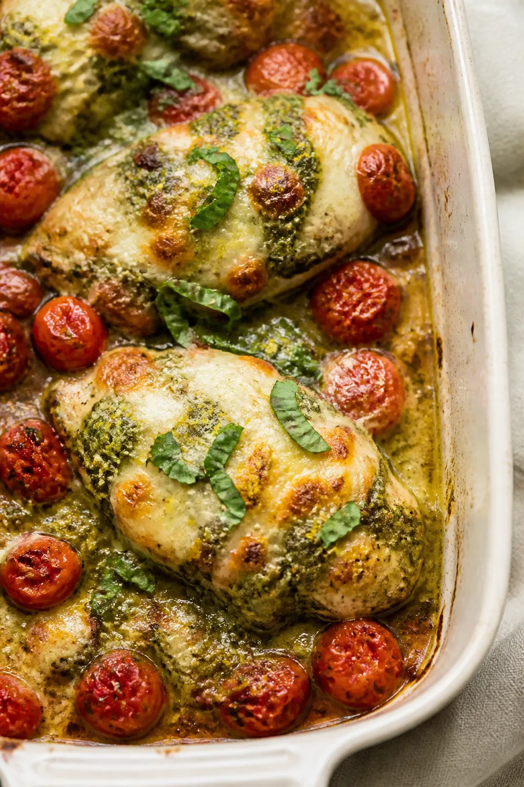 Close-up detail shot of the baked pesto chicken just out of the oven: golden, bubbly mozzarella with
