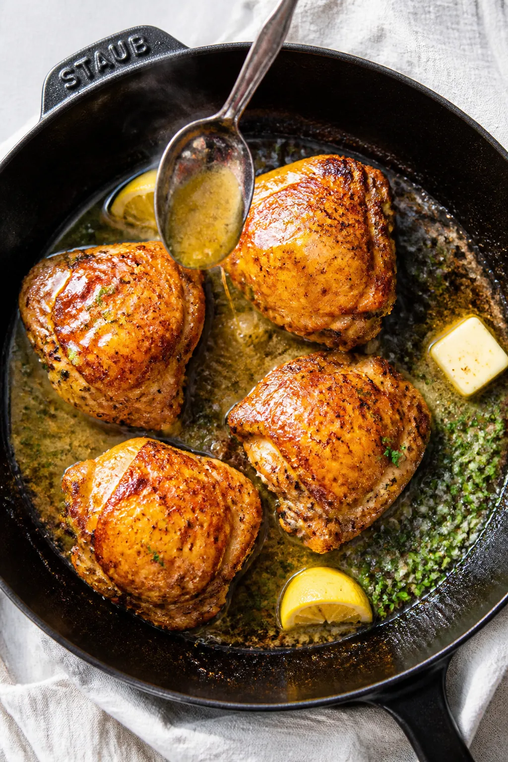 Cooking process action: Overhead shot of chicken thighs mid-sear, flipped skin-side up while a spoon