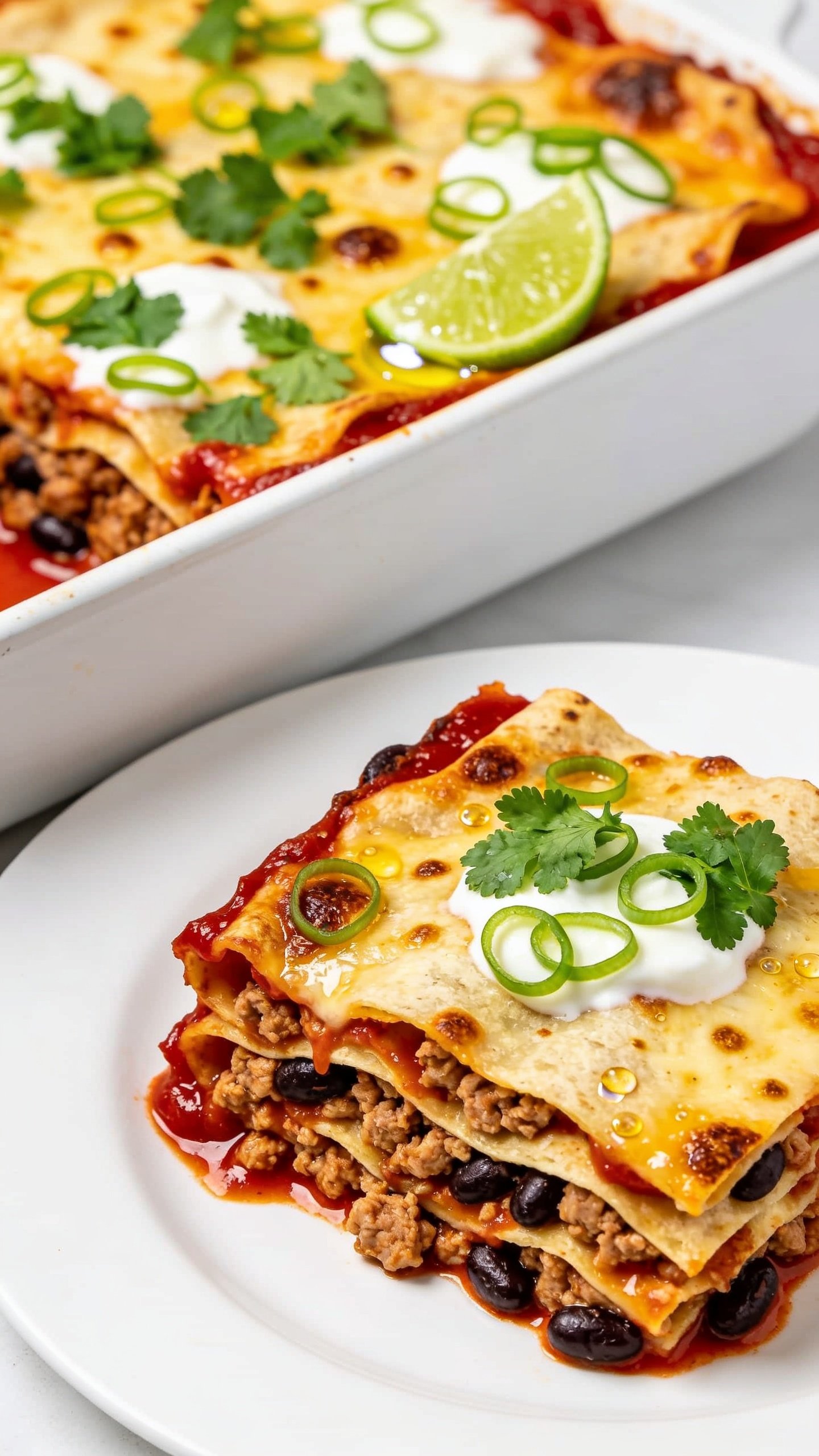 Tight 45-degree angle close-up of a neatly scooped square from the same enchilada bake on a simple white plate beside the pan: visible layered tortillas, juicy ground turkey and black beans, glossy red enchilada sauce seeping at the edges, golden-brown melted cheese with crisped corners, micro-puddles of creamy yogurt integrated, topped with fresh cilantro and thin green onion curls. A squeeze of lime glistens on the surface, tiny bubbles and browned cheese freckles in focus. Bright natural light, shallow depth of field, food filling 90â95% of frame, clean, modern food-blog styling.