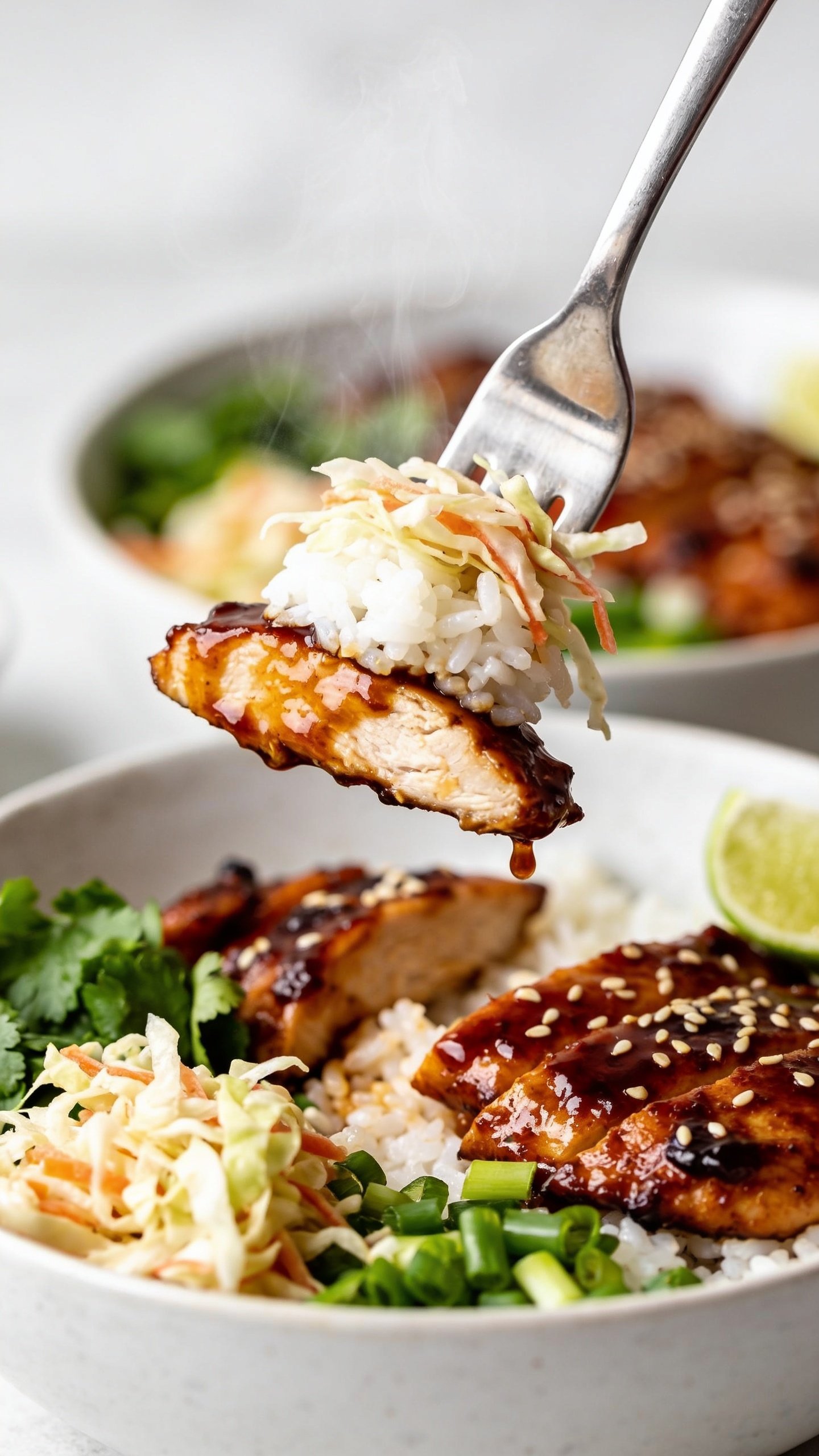 Dynamic action close-up: a stainless fork lifting the perfect bite from the same BBQ Chicken Rice Bowlâone glistening slice of BBQ chicken with glossy sauce clinging and a tiny drip mid-fall, a tuft of fluffy white rice, and a few strands of crunchy slaw; steam subtly rising; background shows the rest of the bowl blurred but clearly matching the hero (same chicken, rice, slaw, cilantro, green onions, sesame, lime wedge); bright natural light highlights the sauce sheen; extremely shallow depth of field isolating the lifted bite; no hands visible, only the fork tip; 90â95% frame dominated by the bowl and lifted bite, capturing motion and irresistible anticipation.