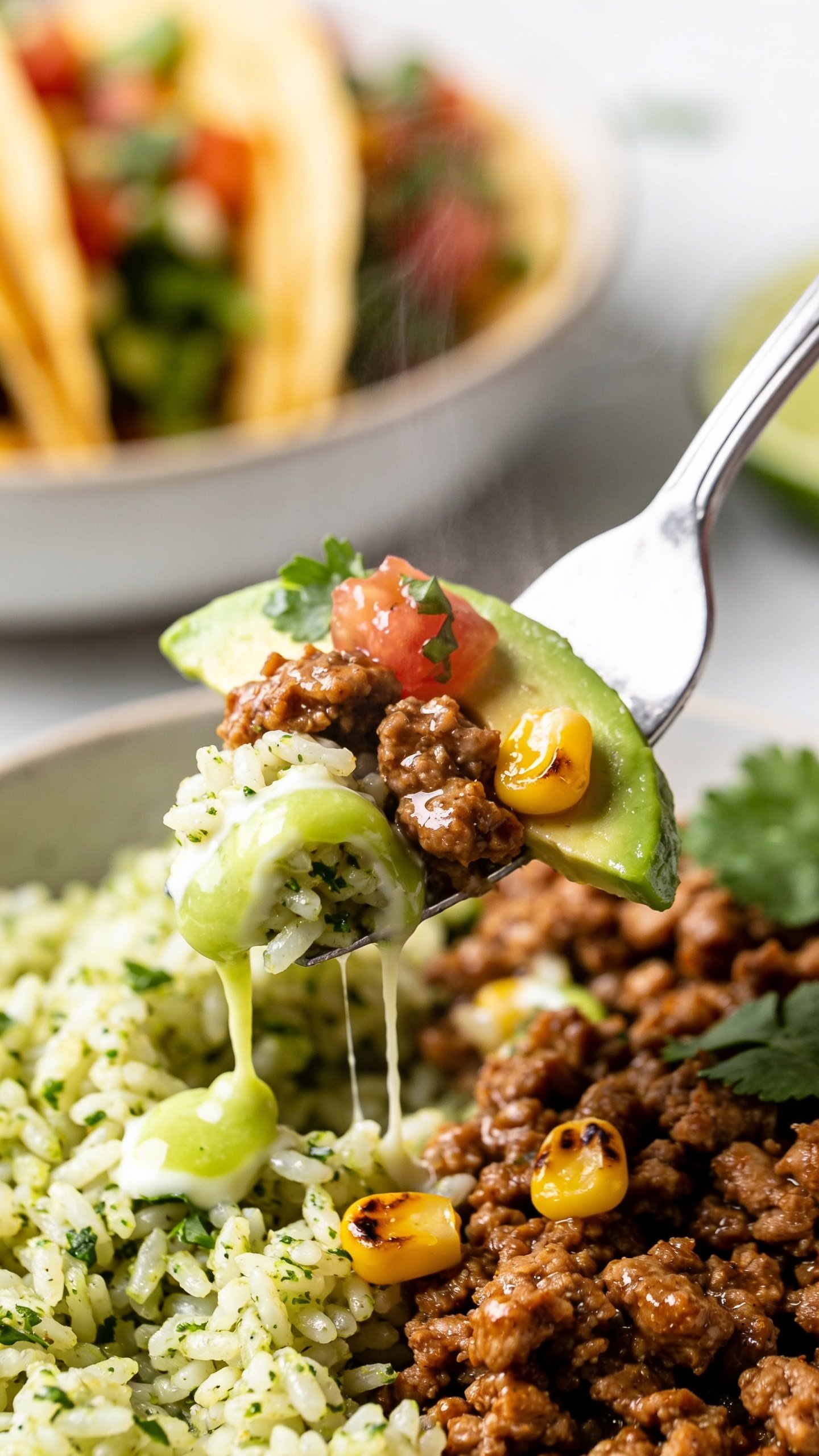 Dynamic action close-up capturing the single most irresistible bite: a stainless fork lifting the perfect bite from the same taco bowlâjuicy, glossy crumbles of seasoned ground turkey clinging to fluffy cilantro-lime rice, a ribbon of lime crema stretching slightly, a sliver of avocado, a roasted corn kernel or two, and a fleck of pico de gallo and cilantro; background shows the bowl blurred but recognizable with the same toppings; bright natural lighting, shallow depth of field, steam faintly visible; motion frozen one second before the bite reaches the mouth; food fills 90â95% of frame; no hands, only the fork tip visible; rich textures, vibrant colors, and premium magazine-quality styling.